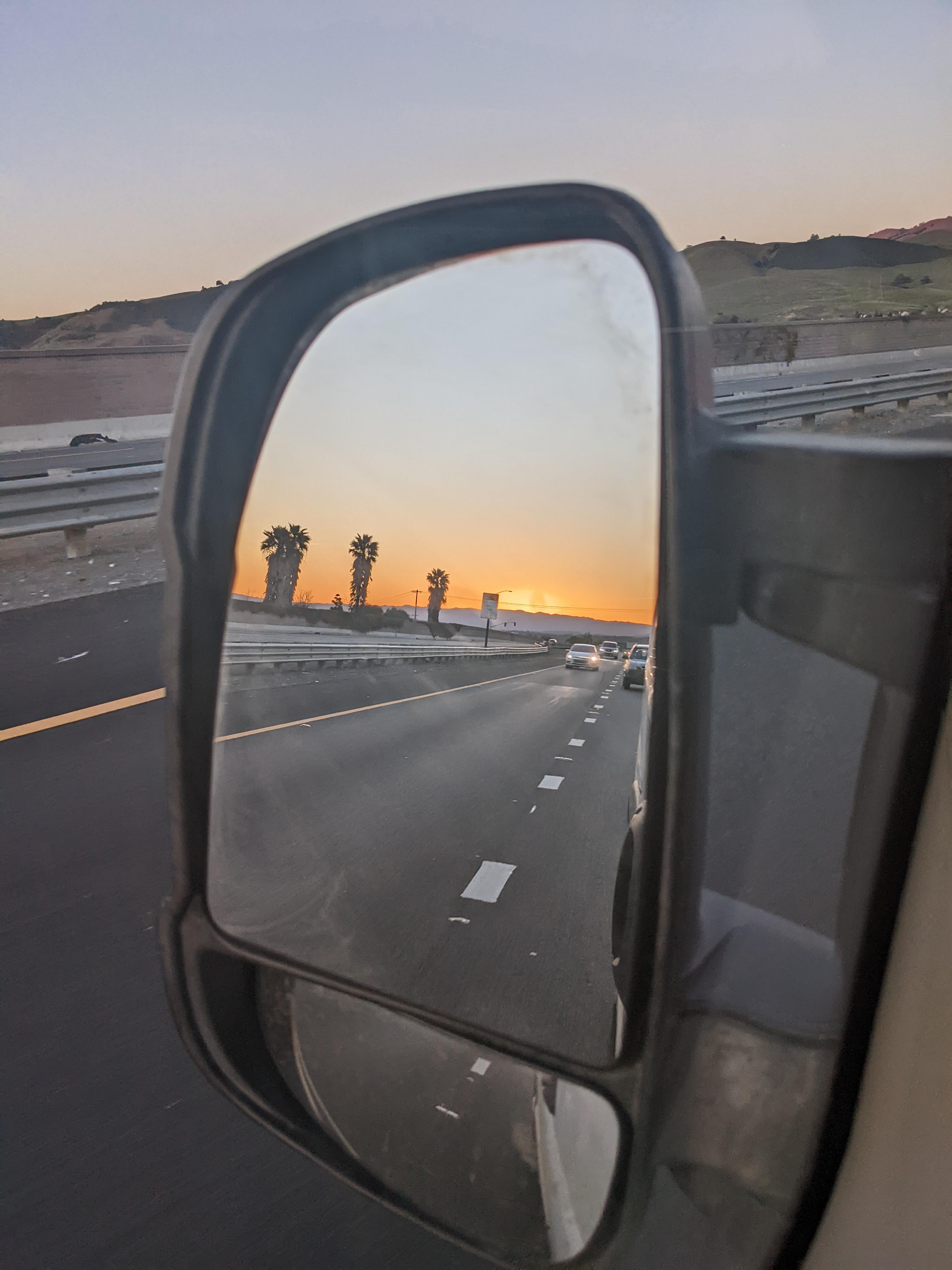[image of a van mirror reflecting a vivid sunset with a palm tree lined highway]